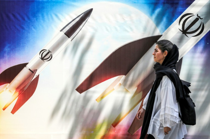 A woman walks past a banner depicting missiles bearing the emblem of the Islamic Republic of Iran in central Tehran