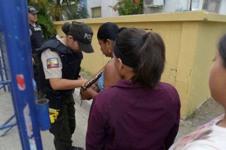 A police officer frisks a woman at the entrance to a polling station in Olon, Ecuador on April 21, 2024