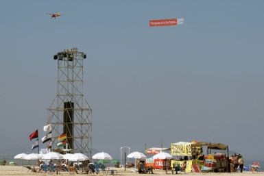 An aircraft carrying a banner saying 'The Queen is in the Palace' is seen flying over the stage at Copacabana Beach