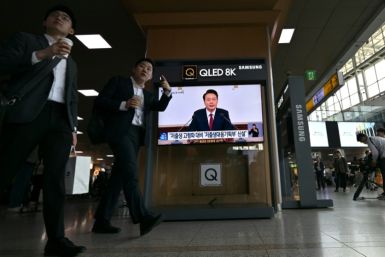 People at a Seoul railway station walk past a screen carrying live footage of South Korean President Yoon Suk Yeol's Thursday press conference