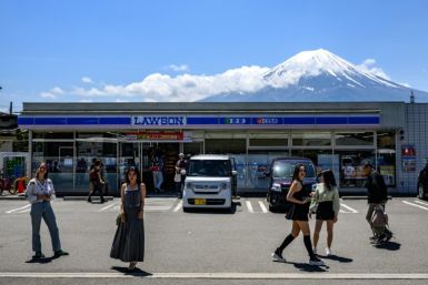 Tourists pose in front of a convenience store with Mount Fuji on May 3, 2024, before a huge black barrier which will be installed to block Mount Fuji from view