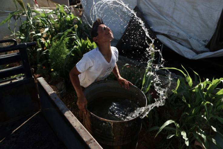 A Syrian youth cools off as he dips his head in a water barrel
