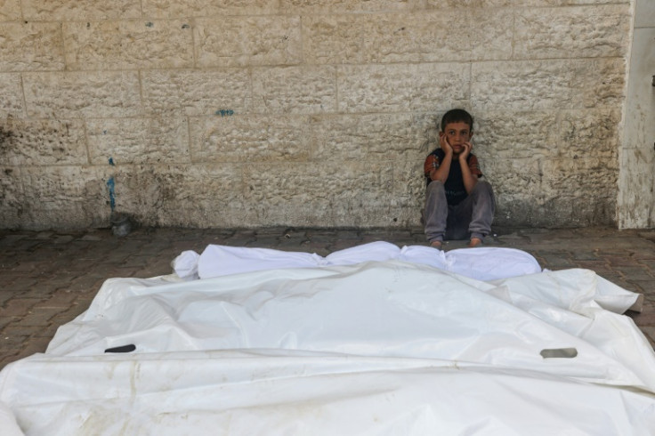 A child sits beside the shrouded corpses of people killed in an Israeli strike, in the yard of the Al-Aqsa Martyrs hospital in Deir el-Balah in the central Gaza Strip