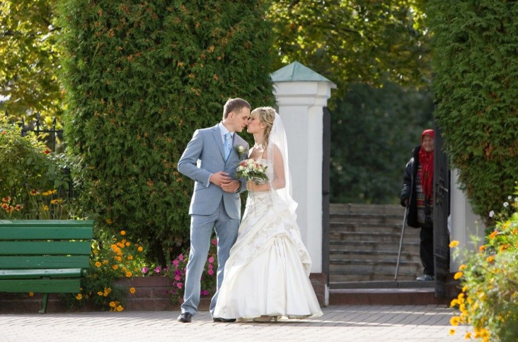 The newly married couple kiss as an elderly woman watches on them in Minsk