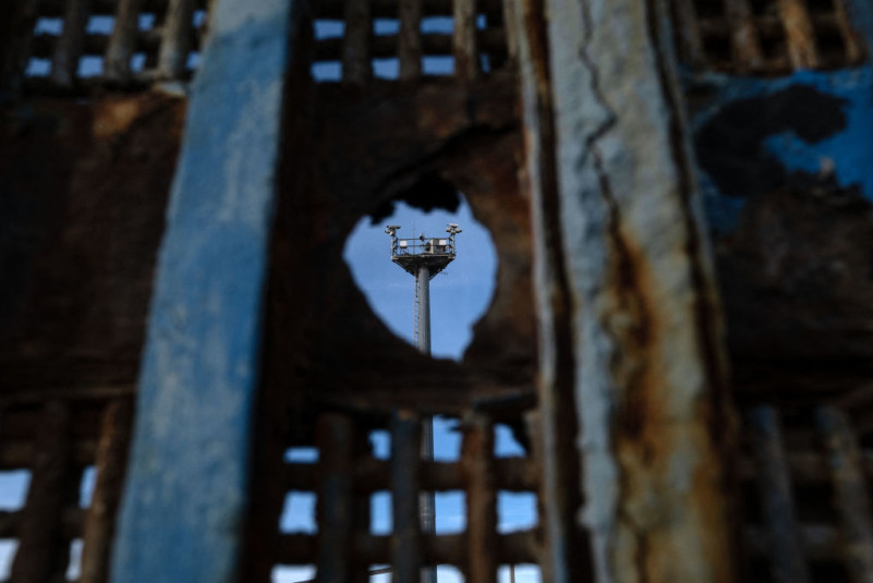 Surveillance tower seen through hole on border wall (2023)