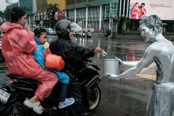 Street performer Ari Munandar, his body painted silver, receives a tip in the rain at an intersection in Jakarta
