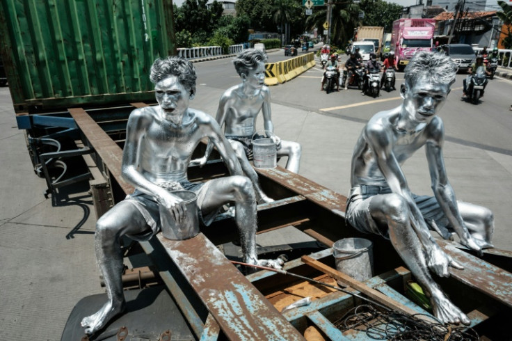 Street performers Keris Munandar (R), his brother Ari Munandar (L), and their neighbour Riyan Ahmad Fazriyansah hitch a ride on the back of a container truck to reach an intersection in Jakarta