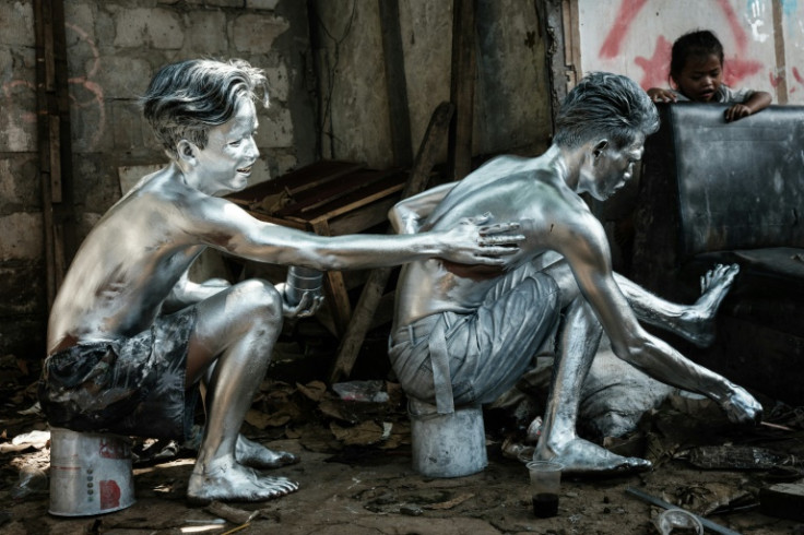Street performers Keris Munandar (R) and his neighbour Riyan Ahmad Fazriyansah paint their bodies silver in Jakarta
