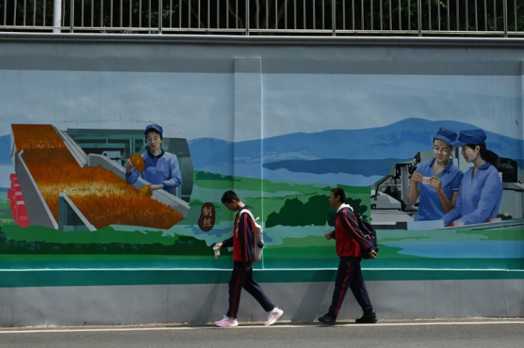 Students walk past a mural of workers at a cigarette factory in Yuxi, China