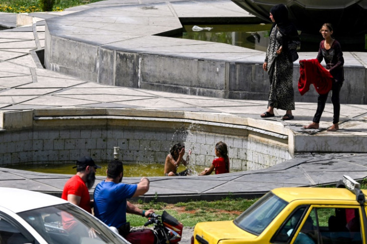 Motorists drive past as Syrian children play at a water fountain in Sabaa Bahrat Square in Damascus
