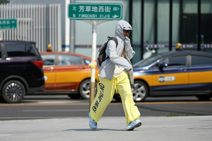 A woman wearing sun protective clothing crosses a street in Beijing on June 23, 2025. Beijing residents sought shade and cooled off in canals on June 23 as the Chinese capital sweltered in its hottest day of the year so far.