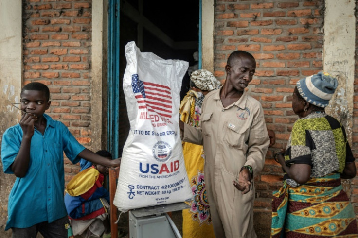 A Burundian government official speaks with newly arrived Congolese refugees while weighing a sack of rice from the final batches delivered by the now-dismantled United States Agency for International Development