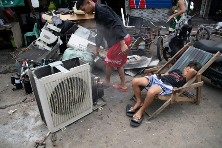 A child sleeps on a deckchair as workers empty coolant from a discarded air conditioning unit