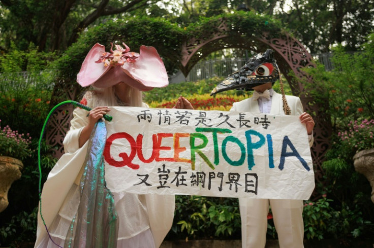 Non-binary performance artist Holok Chen (L) holds a banner reading: "If the love is meant to endure, why should it be confined to portals and digital boundaries"
