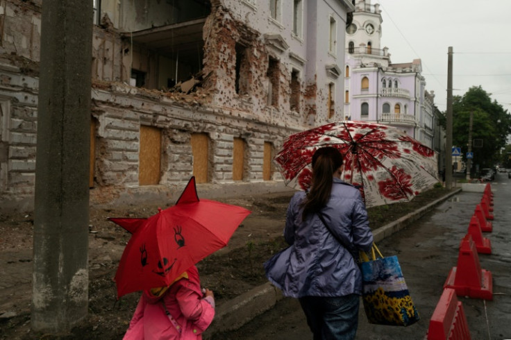 Residents pass the facades of historic buildings that were damaged by missiles