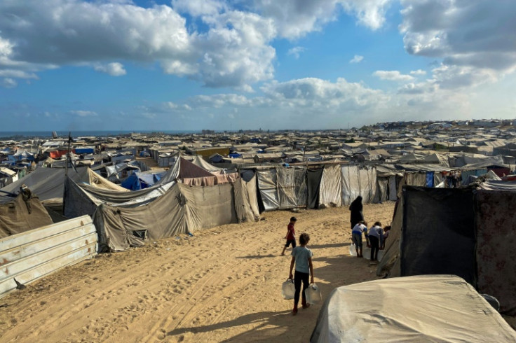 Palestinian children carry water past line after line of tents housing displaced families in the sand dunes of Mawasi on Gaza's Mediterranean coast.