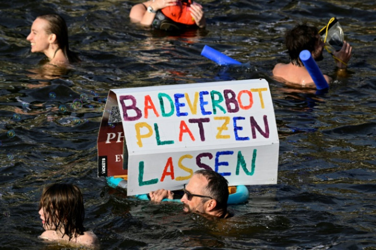 A participant swims with a placard with the slogan 'Let the bathing ban fall' while taking a dip in the Spree river during a swimming demonstration for the abolition of the general swimming ban in the inner-city Spree river in central Berlin on August 12,
