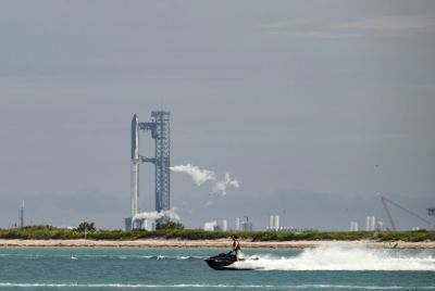 A person drives a jet ski as SpaceX's Starship is seen on a launchpad in the distance near Starbase, Texas, on August 24, 2025