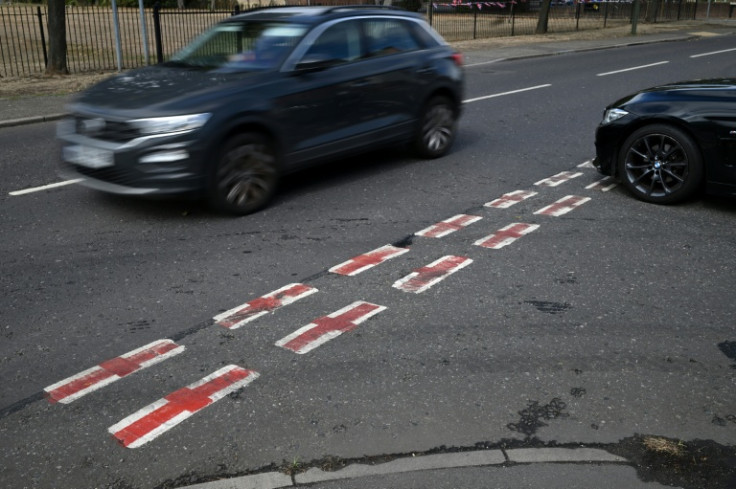 Cars pass St George's Cross flags, the national flag of England, painted onto the white of road markings near a London residential street