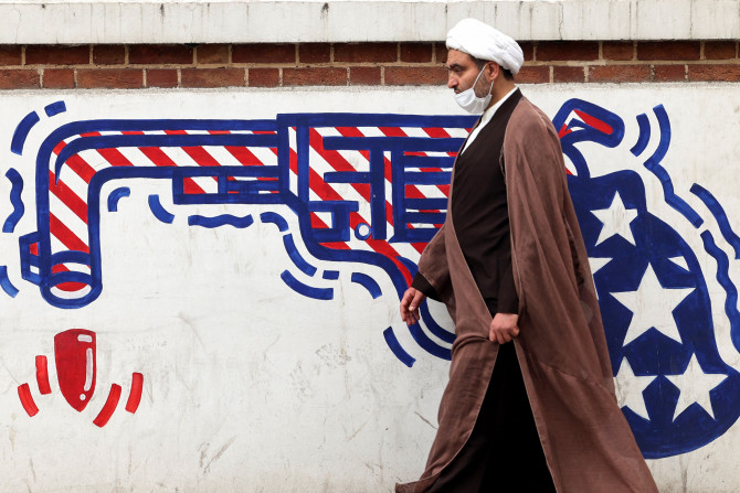 An Iranian cleric walks past an anti-US mural