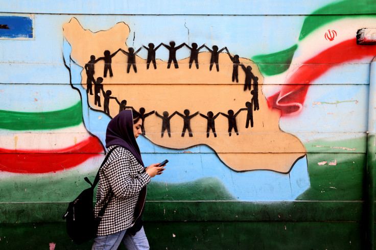 A woman walks past the flag and map of Iran