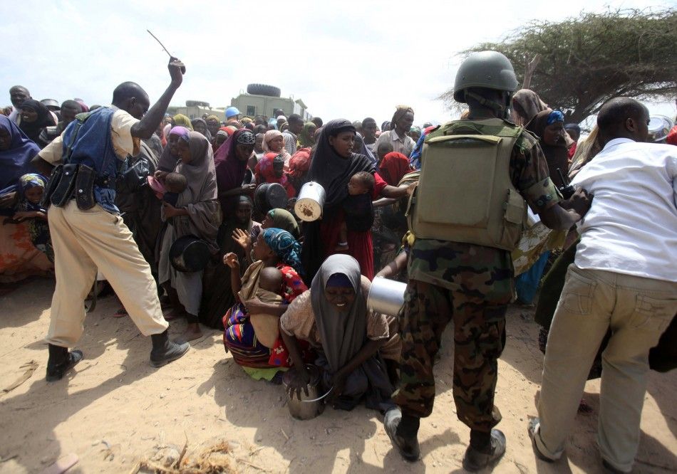 Somali government soldiers stand guard over internally displaced people as they wait for food aid at a camp in the capital Mogadishu