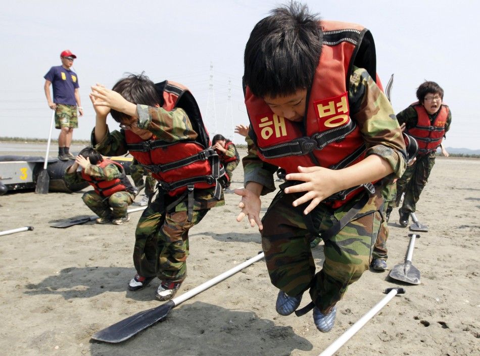 Elementary school students jump over paddles as they participate in a summer military camp for civilians at the Cheongryong Self-denial Training Camp run by retired marines in Ansan