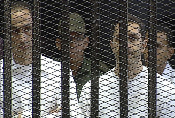 Alaa and Gamal Mubarak stand in the courtroom during their trial at the Police Academy in Cairo