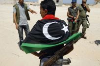 Libyan rebels, one wearing a Kingdom of Libya flag, walk around the Ras Jdir border post on the border with Tunisia