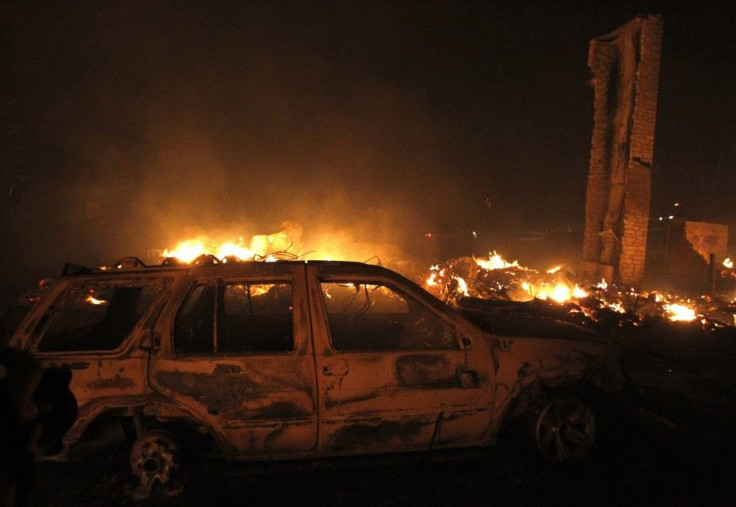 A burnt car sits in front of a house that has been razed to the ground as a wildfire burns out of control near Bastrop