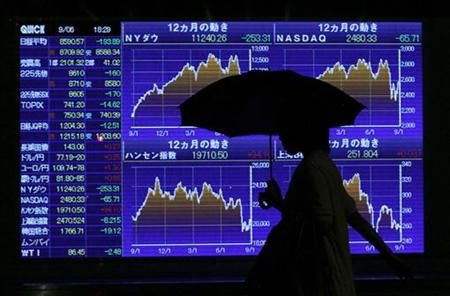 Woman walks past an electronic board displaying market indices outside a brokerage in Toky