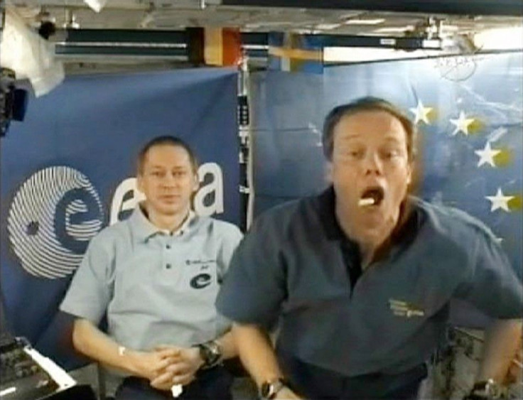 European Space Agency astronaut Christer Fuglesang catches some food in his mouth as fellow ESA astronaut Frank De Winne looks on