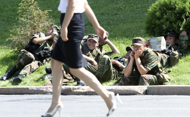 Army servicemen sit on the ground as they watch a woman walk past, while waiting for instructions, during a rally near the parliament headquarters in Bishkek