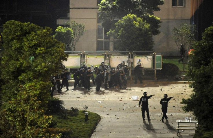 Riot policemen shield themselves from rocks thrown by protesters they approach the entrance of a factory in Haining