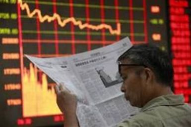 An investor reads a newspaper in front of an electrical board showing stock information at a brokerage house in Huaibei