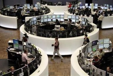 Traders work at their desks in front of the DAX index board at Frankfurt&#039;s stock exchange