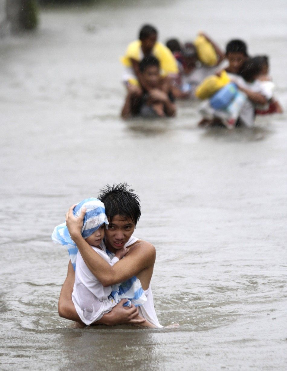 A resident carries his son while crossing on waist deep floodwaters brought by Typhoon Nesat, locally known as Pedring, that hit the Tanza town of Malabon city 27092011