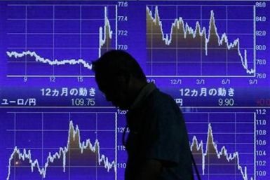 Man looks down as he walks past an electronic board displaying market indices outside a brokerage in Tokyo