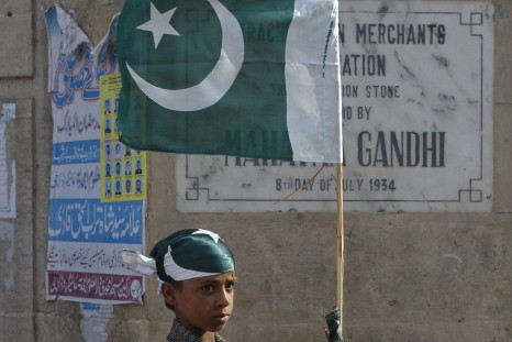 A boy ties up a Pakistan national flag to a bamboo stick as some of nearly a dozen traders near by taking part in an anti-American demonstration in Karachi