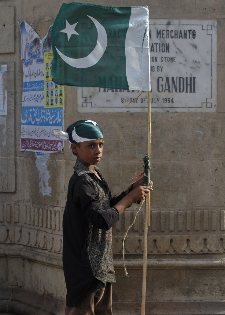 A boy ties up a Pakistan national flag to a bamboo stick as some of nearly a dozen traders near by taking part in an anti-American demonstration in Karachi