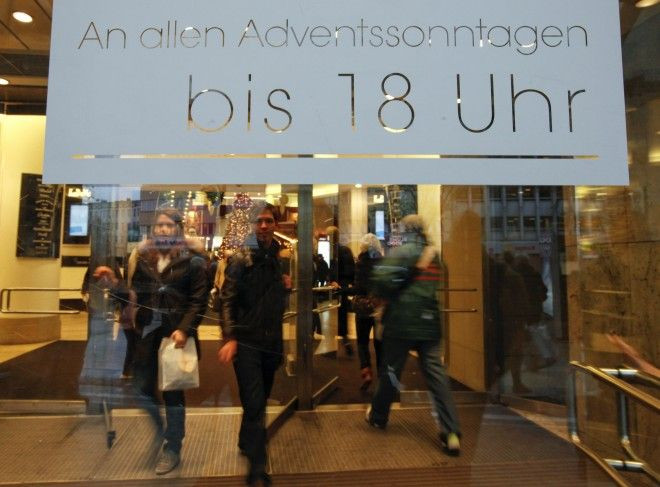 Shoppers walk towards the main entrance with a sign announcing the opening hours of Berlin's famous KaDeWe department store.