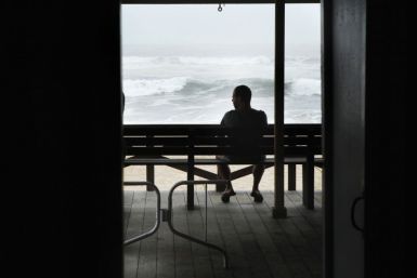 A man sits on a bench to watch waves pushed onto Long Island by the winds of Hurricane Irene in East Hampton Village, New York