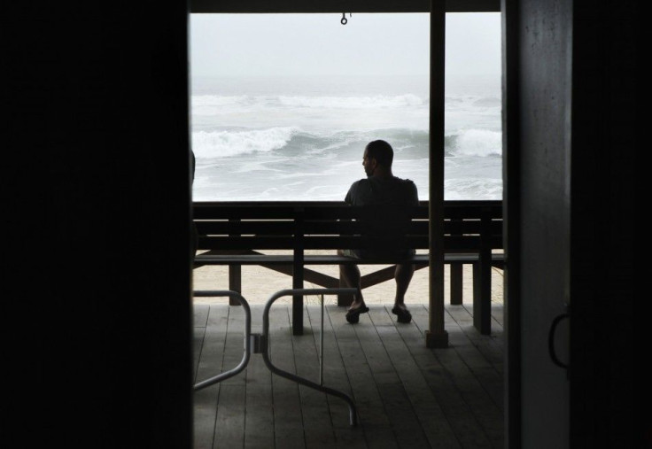 A man sits on a bench to watch waves pushed onto Long Island by the winds of Hurricane Irene in East Hampton Village, New York