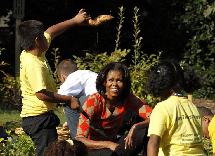 U.S. first lady Michelle Obama looks at a sweet potato pulled out by a local school child as they harvest the White House Kitchen Garden during the fall season in Washington