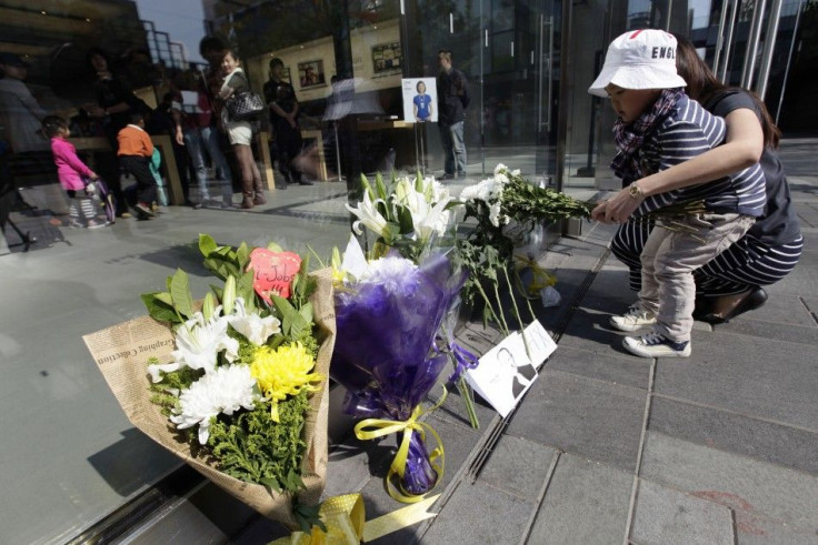 A woman and her child place flowers for Jobs next to entrance of Apple retail store in Beijing's Sanlitun