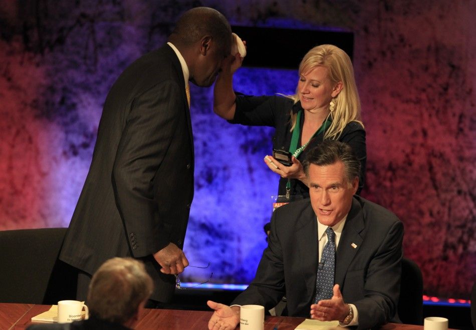 A makeup artist applies powder to the head of Republican presidential candidate businessman Herman Cain L as former Massachusetts Governor Mitt Romney R talks with debate moderator Charlie Rose Lower L during a break in the Republican presidential d