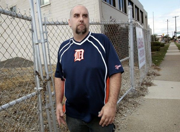 Scott Stevenson stands outside the locked gate of a shuttered small manufacturing plant