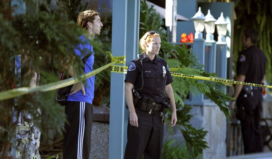 Police officer and bystander stand near police tape near Salon Meritage following a shooting that left six people dead and three injured in Seal Beach