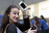 A customer shows off her new iPhone 4S as she leaves an Apple Store in New York
