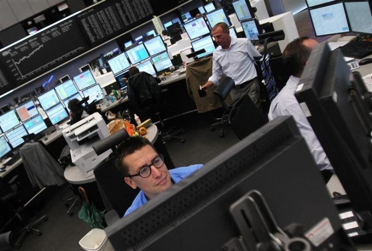 Traders are pictured at their desks in front of the DAX board at the Frankfurt stock exchange